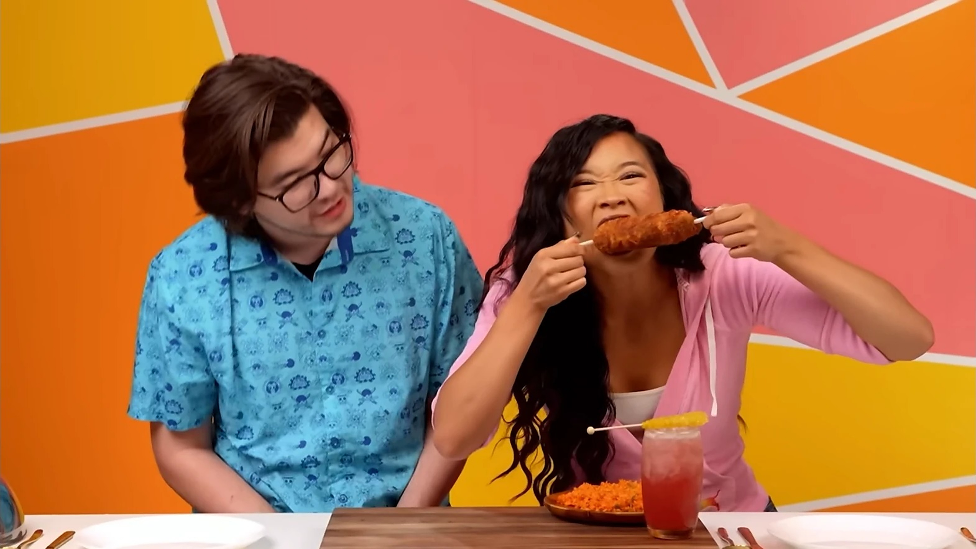 Kamryn Hernandez biting into a corn dog on camera with a co-host beside her